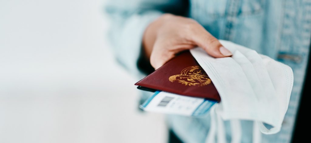 Urlaub planen in Zeiten von Corona: Was ist 2021 noch möglich? Person hält Reisepass, Tickets und eine medizinische Maske in der Hand.