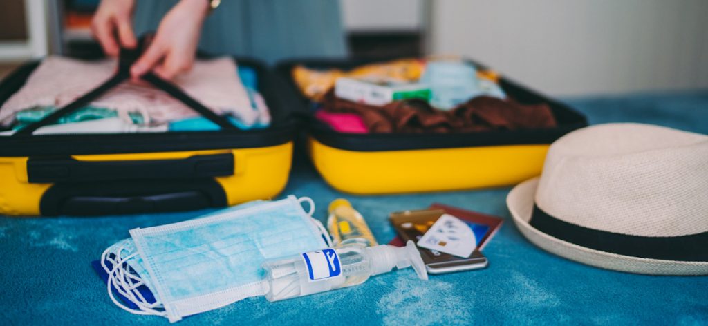 Urlaub planen in Zeiten von Corona: Was ist 2021 noch möglich? Person packt Urlaubskoffer, u.a. mit medizinischen Masken und Desinfektionsmittel.