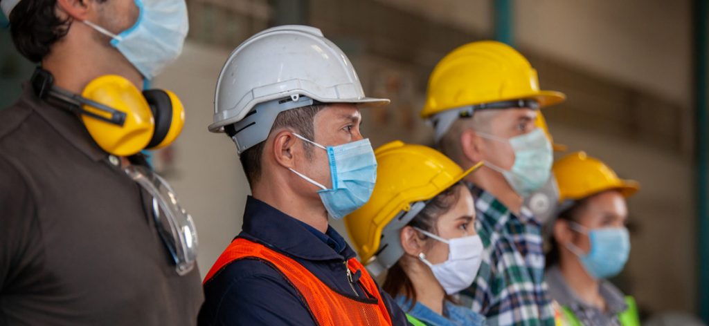 Handwerker und Handwerkerinnen mit Schutzhelm und medizinischen Masken