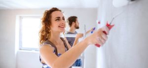 Glückliche junge Frau streicht Zimmerwand