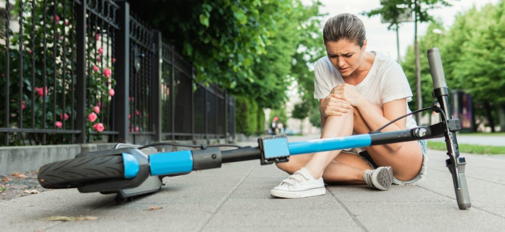 Junge Frau hält sich ihr Knie, nachdem sie mit dem E-Scooter gestürzt ist