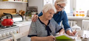 Ältere Frau unterschreibt Papiere, während jüngere Frau ihr über die Schulter schaut