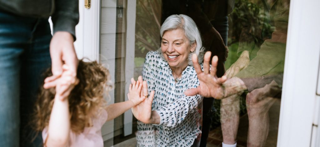 Oma sieht ihre Enkelin durch Fensterscheibe und freut sich