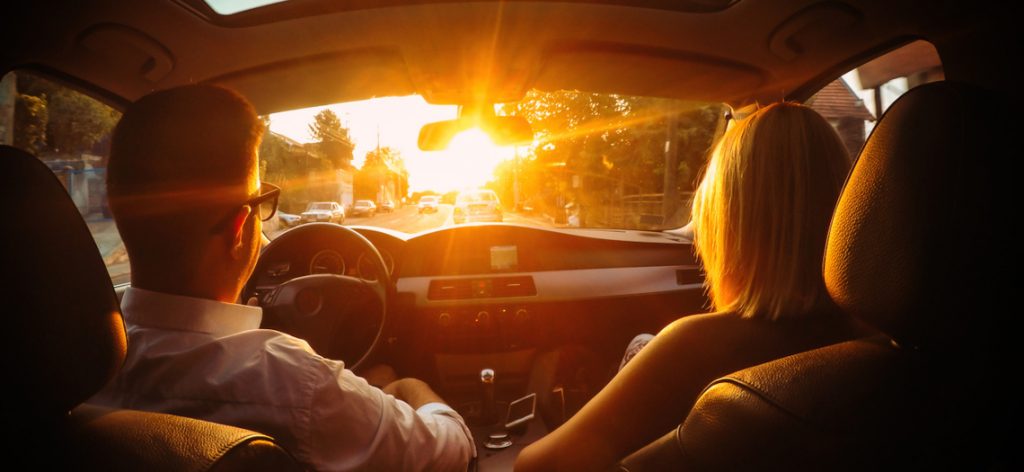 Junges Paar fährt im Auto in den Sonnenuntergang.