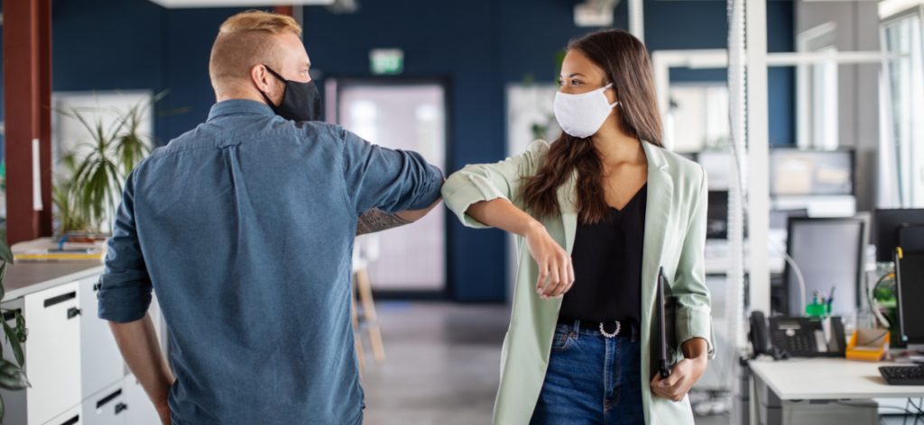 Zwei Arbeitskollegen mit Masken begrüßen sich mit dem Ellbogen.