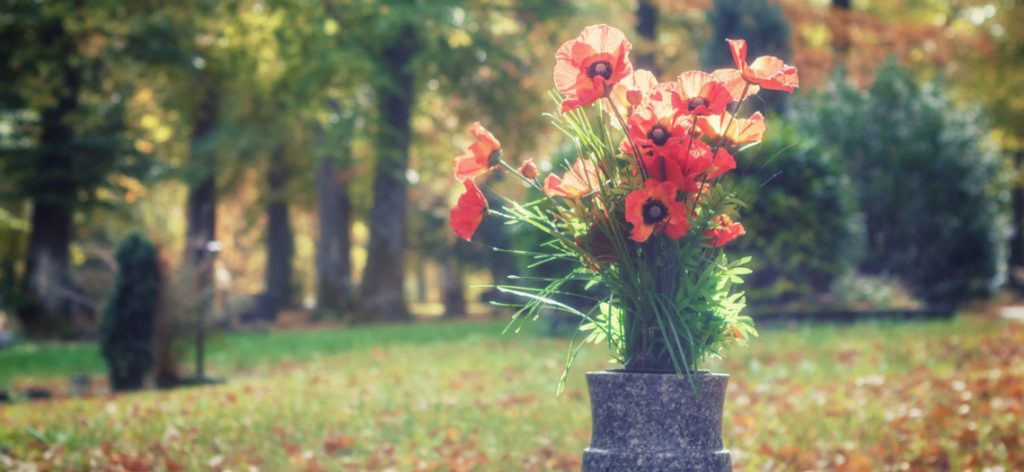 Ein Strauß roter Mohnblumen steht in einer Vase auf einem Grab.