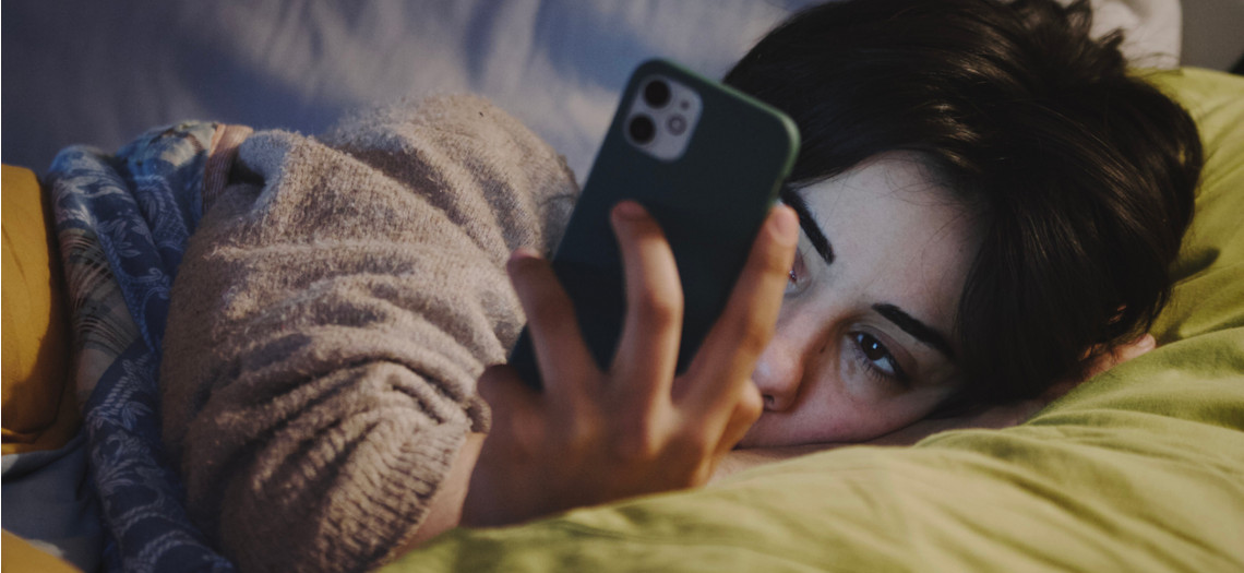 Traurige Frau im Bett mit Handy