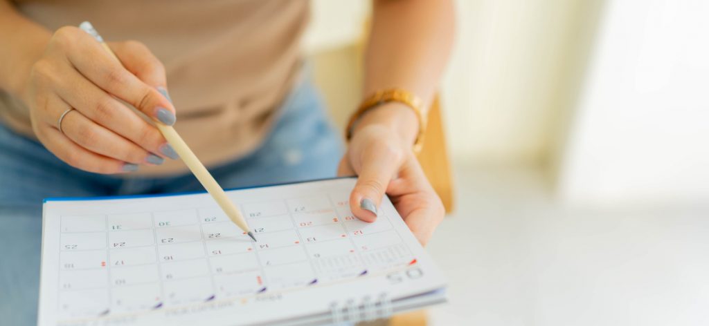 Eine Frau schreibt mit Bleistift in ihren Tisch-Kalender.