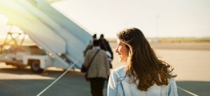 Junge Frau läuft im Sonnenschein zur Eingangstreppe eines Flugzeugs.