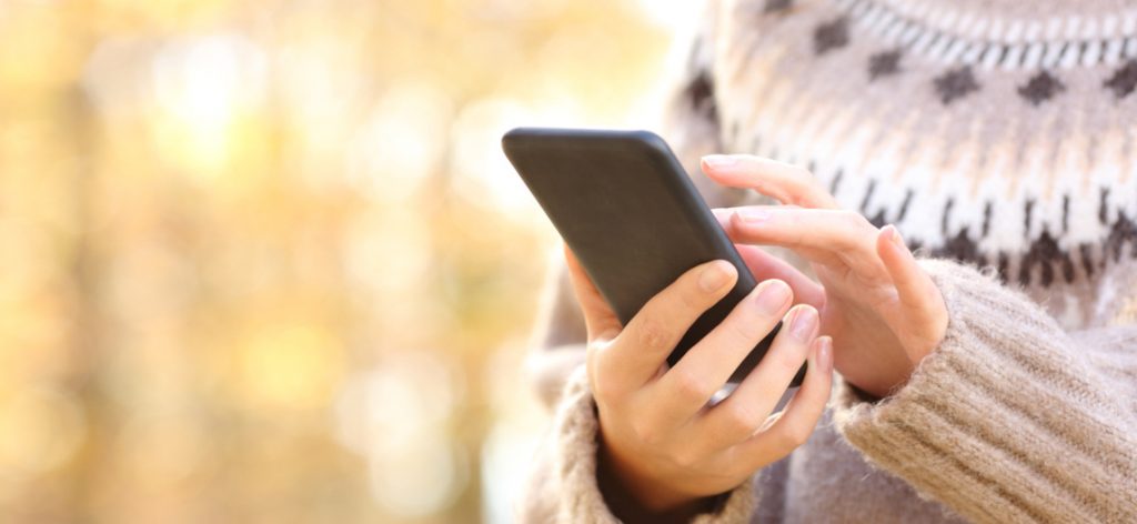 Frau mit Winterpullover tippt auf einem schwarzen Smartphone.