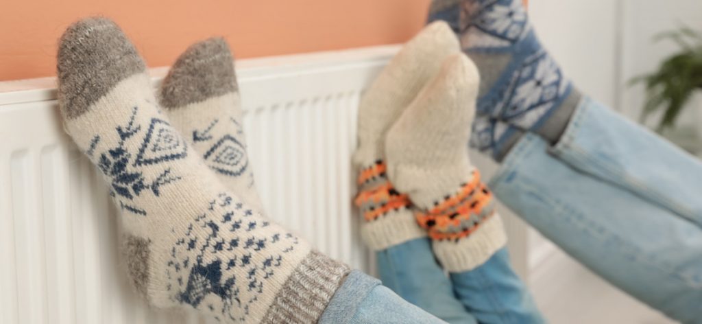 Familie hält Füsse in Wintersocken an eine Heizung.