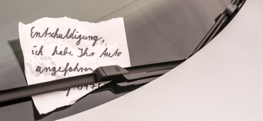 Zettel mit Entschuldigung klemmt unter der Windschutzscheibe eines Autos.