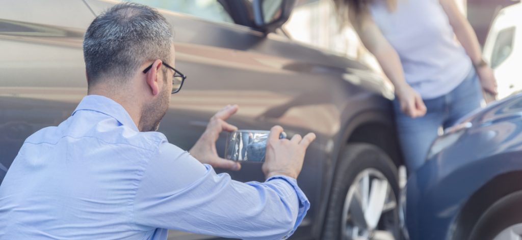 Mann fotografiert den Blechschaden nach dem Zusammenstoß von zwei Autos.