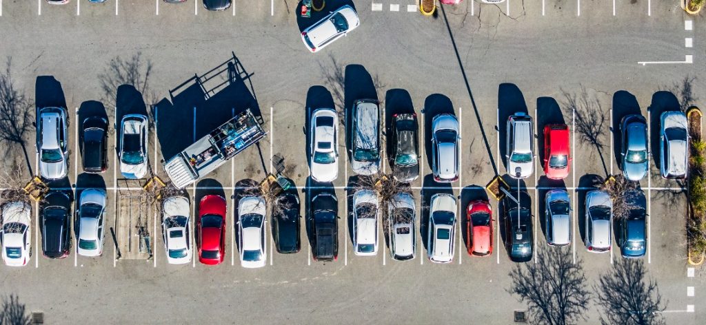 Parkplatz mit Autos aus der Vogelperspektive. Ein Fahrzeug steht quer über drei Stellplätze.