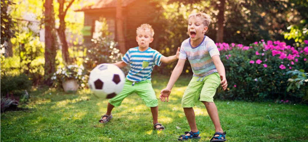 zwei Kinder spielen im Garten Fußball