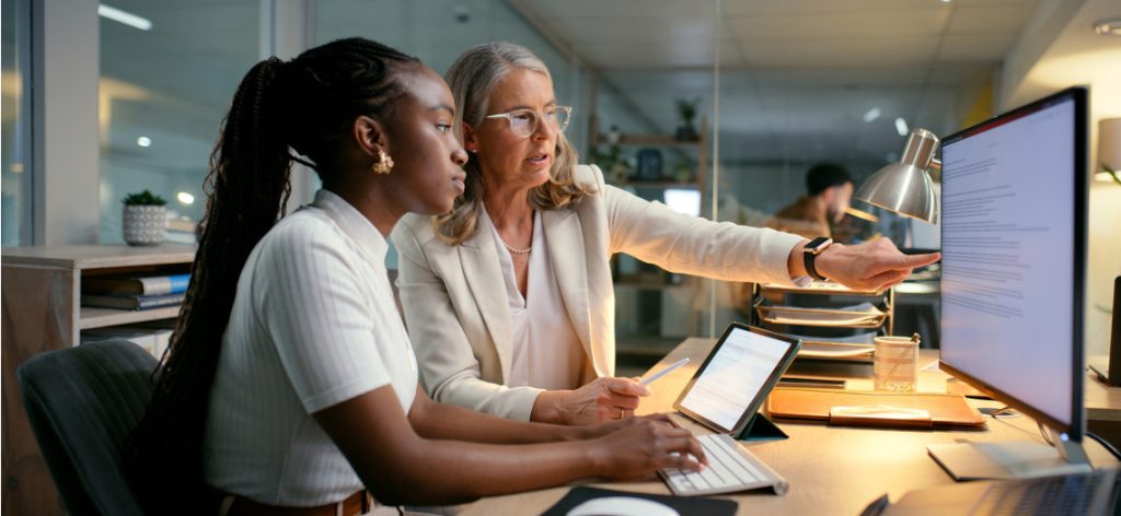 Junge und ältere Frau in Businesskleidung sitzen im Büro am Computer