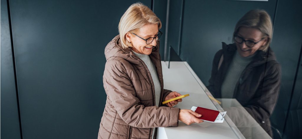 Ältere Frau zeigt an einem Schalter ihren Reisepass und en Ticket