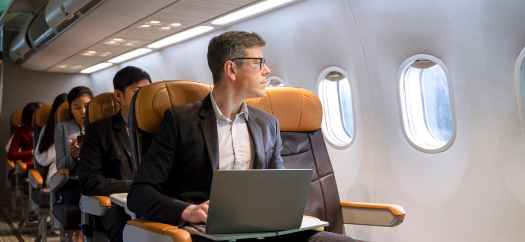 Mann in Businesskleidung sitzt mit Laptop im Flugzeug und schaut aus dem Fenster