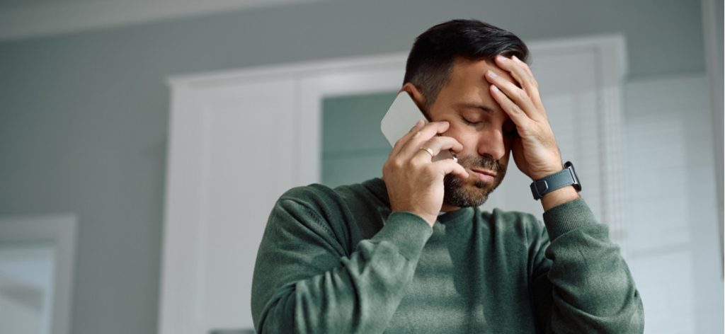 Mann telefoniert verzweifelt am Handy mit Hand am Kopf