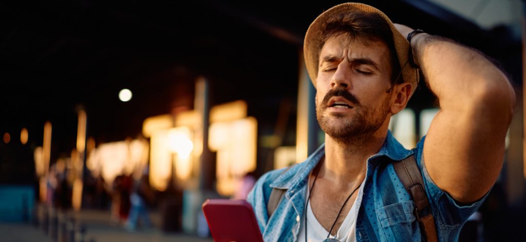 Mann mit Urlaubskleidung in Sonnenlicht Handy in der Hand verzweifelt Hand am Kopf