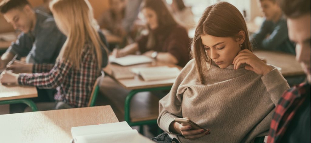 Schülerin schaut im Klassenraum im Unterricht aufs Smartphone