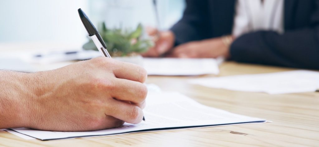 Hand mit Stift unterschreibt Vertrag auf einem Tisch