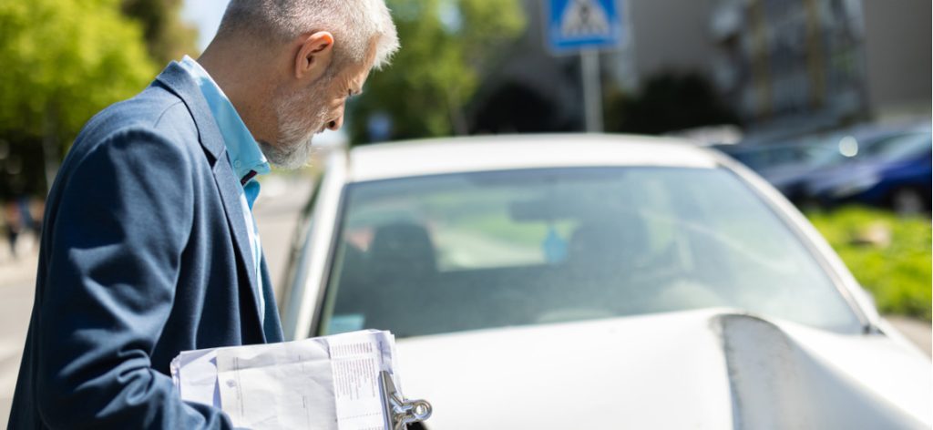 Mann in Anzug mit Klemmbrett an einem Auto