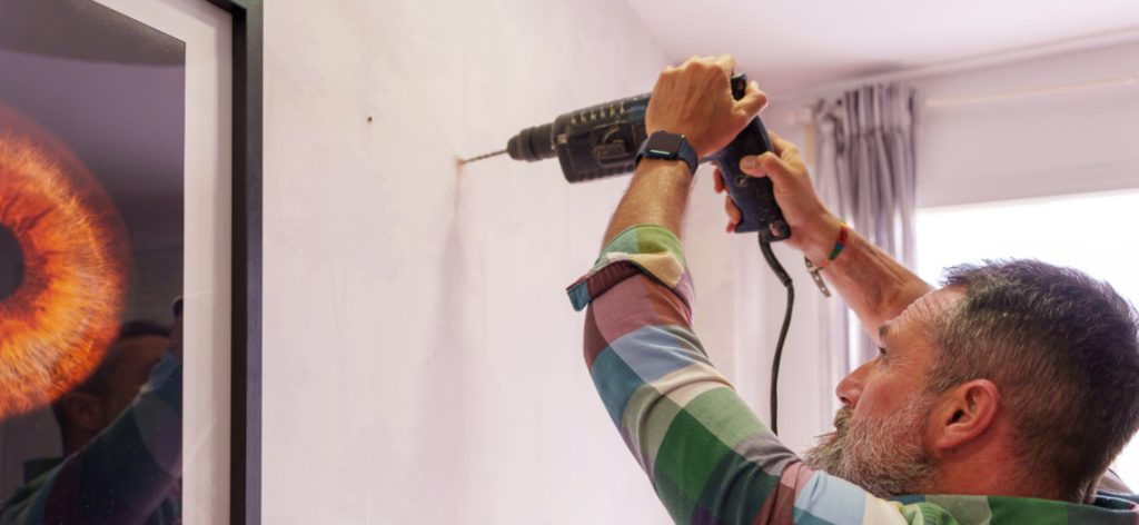 Mann bohrt in einer Wohnung mit einer Bohrmaschine in eine Wand