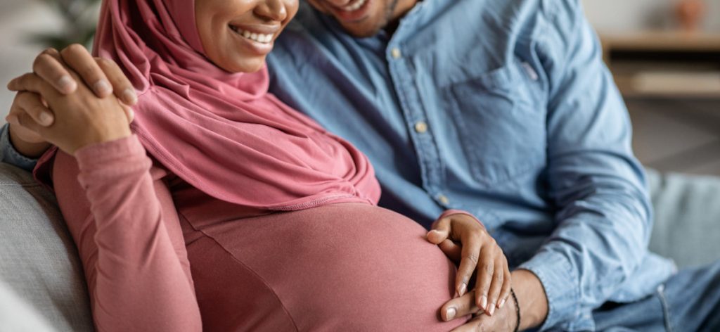 Schwangere Frau und Partner auf Sofa Hand auf dem Bauch