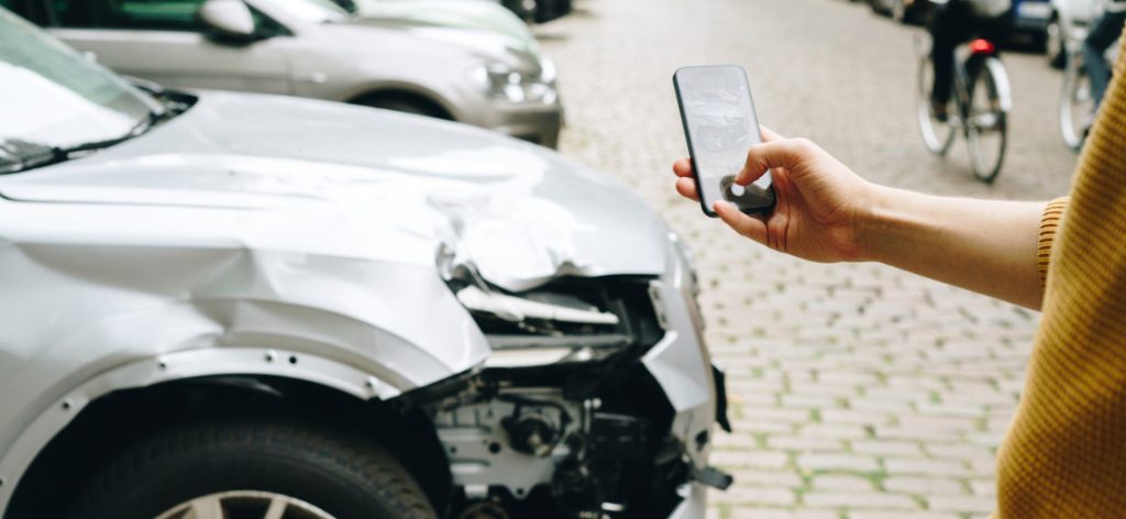 Frau macht mit Smartphone Foto von Schaden am Auto