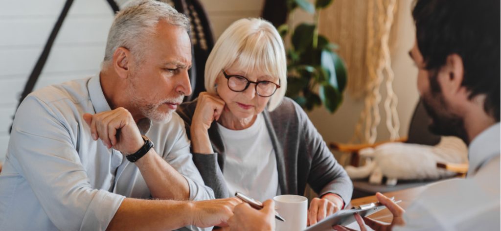 Älterer Mann und ältere Frau sitzen am Tisch mit einem anderen mann und unterschreiben einen Vertrag