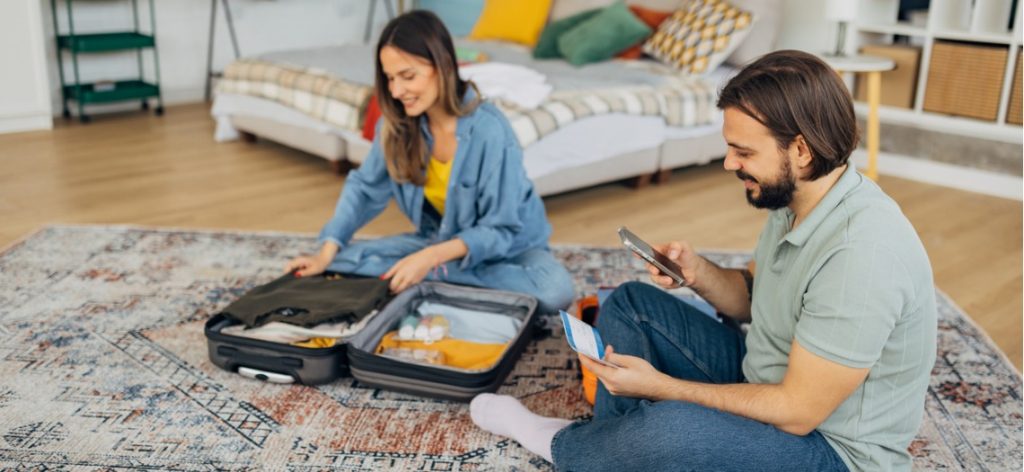 Paar sitzt mit Flugticket in Schlafzimmer auf dem Boden und packt einen Koffer
