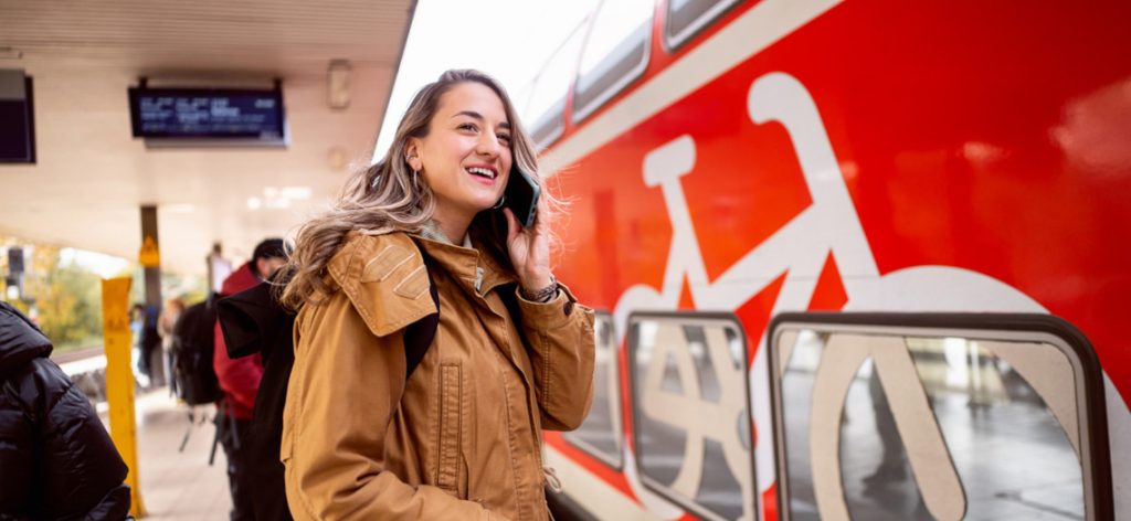 Junge Frau steht telefonierend am Bahnsteig am Zug