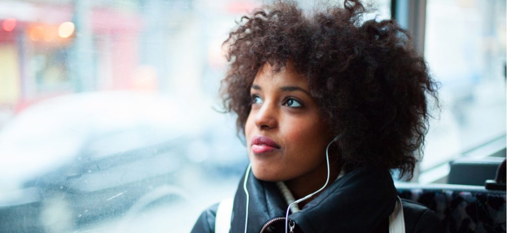 Junge Frau sitzt mit Kopfhörern im Bus und schaut aus dem Fenster
