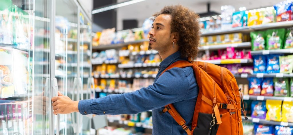 Mann mit Rucksack steht im Supermarkt vorm Kühlregal und öffnet die Tür