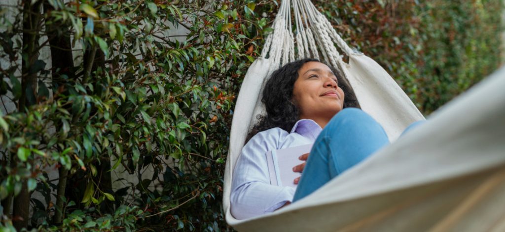 Frau liegt lächelnd mit Buch  in Hängematte