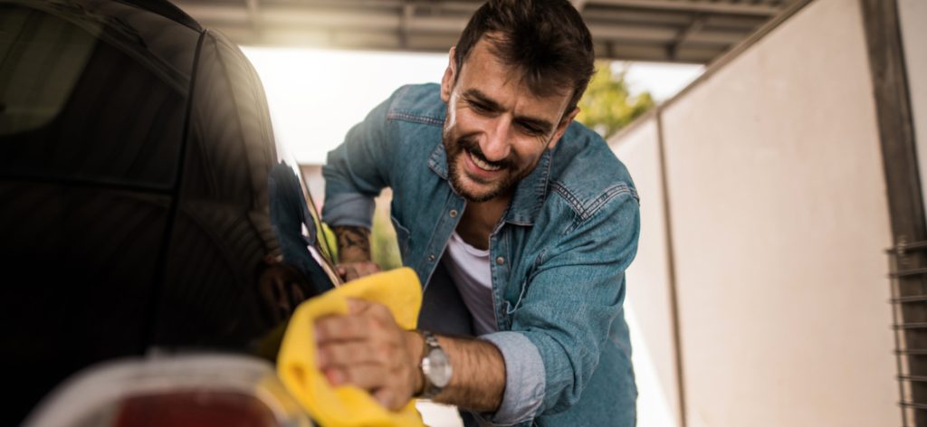 Mann im Jeanshemd wascht lachend mit einem Lappen sein Auto