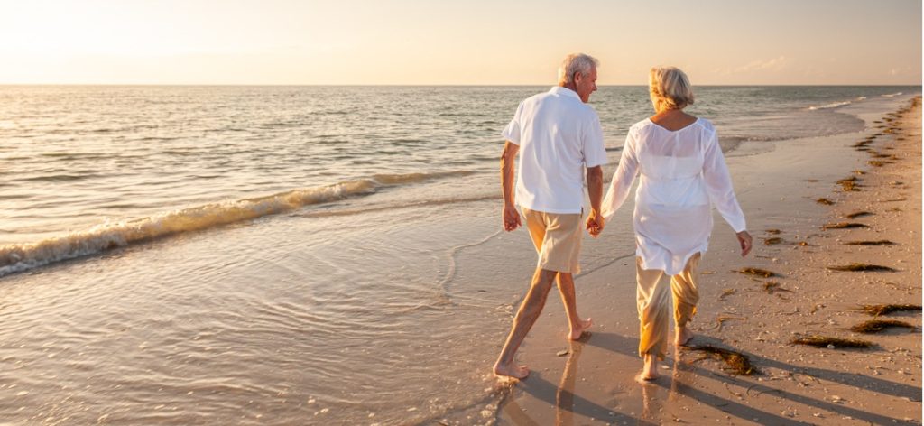 Älteres Paar spaziert Hand in Hand an einem Strand am Meer bei Abendsonne