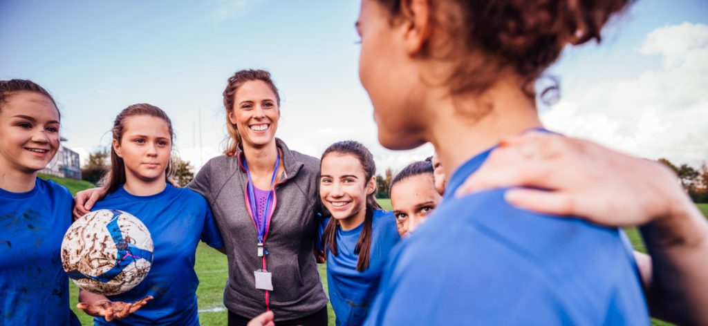 Mädchen-Fußballmannschaft mit Trainerin auf dem Platz in blauen Trikots mit Ball