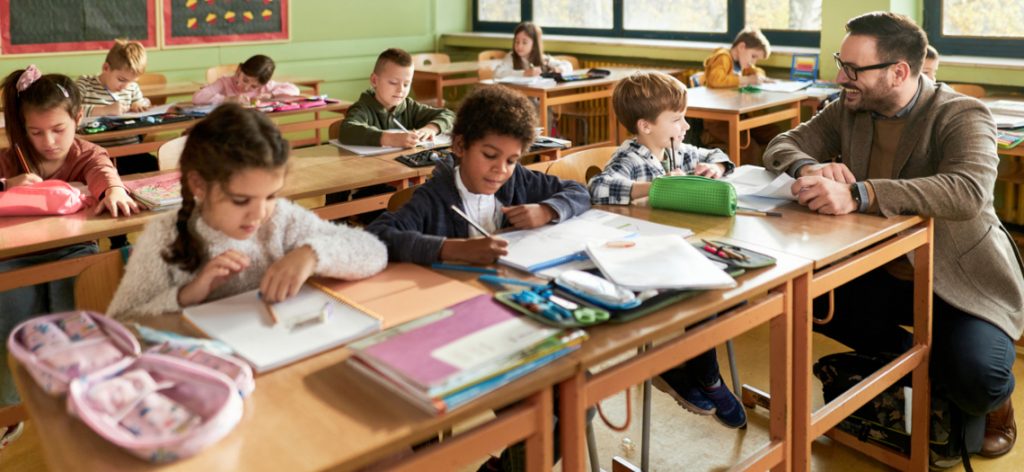 Lachender Lehrer hilft Schüler in Grundschulklasse