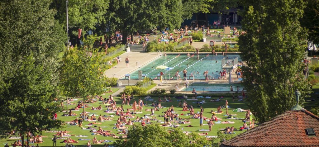 Gute besuchtes Freibad mit vielen Menschen im Becken und auf der Liegewiese
