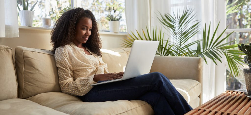 Frau sitzt mit Laptop auf dem Sofa