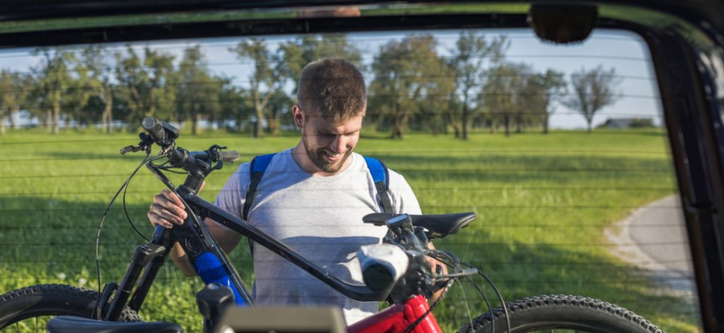 Mann befestigt Fahrrad am Heckgepäckträger eines Autos